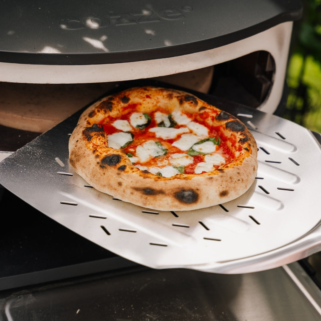 Pizza på pizzaspade på väg ut ur pizzaugn