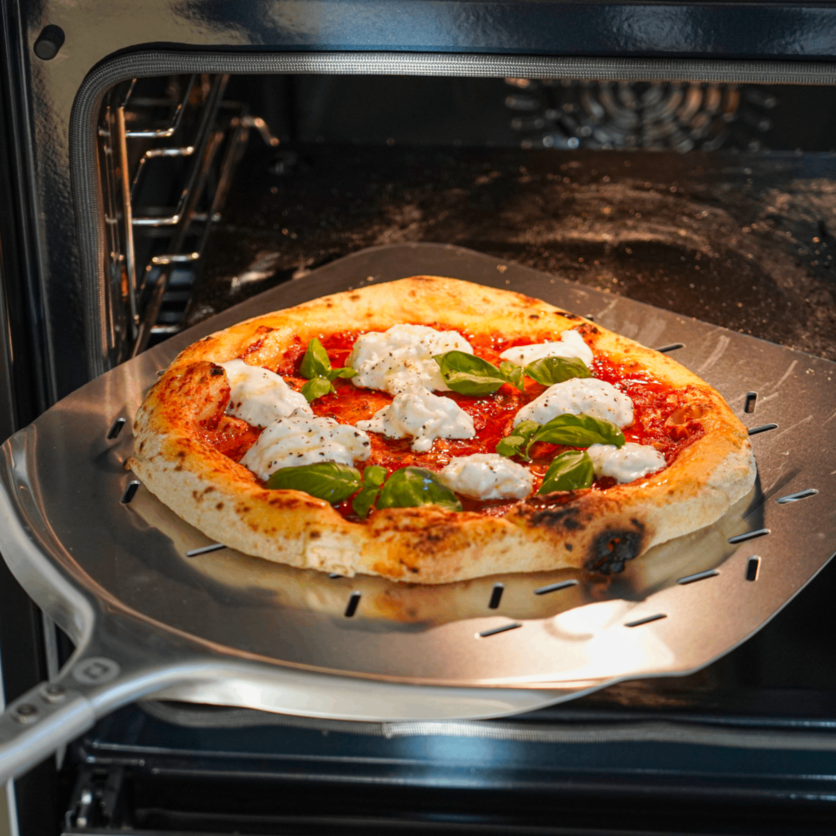Pizza på pizzaspade på väg in i ugnen